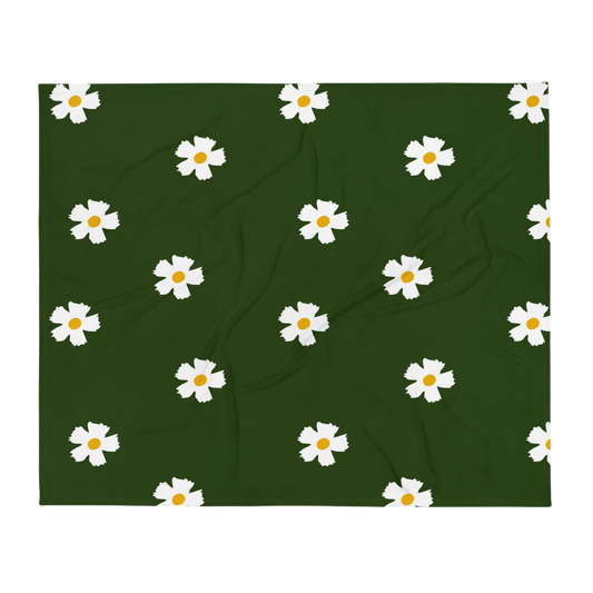 A photo of a rich-toned green blanket patterned with hand-painted white daisies with yellow centres.