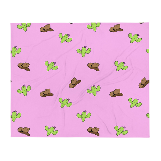 A photo of a soft pink blanket patterned with hand-drawn brown cowboy hats and hand-drawn green cacti with purple flowers.