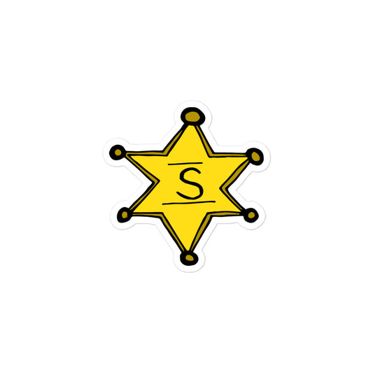 A photo of a yellow Sheriff's badge sticker with an "S" for Sheriff in the centre. 