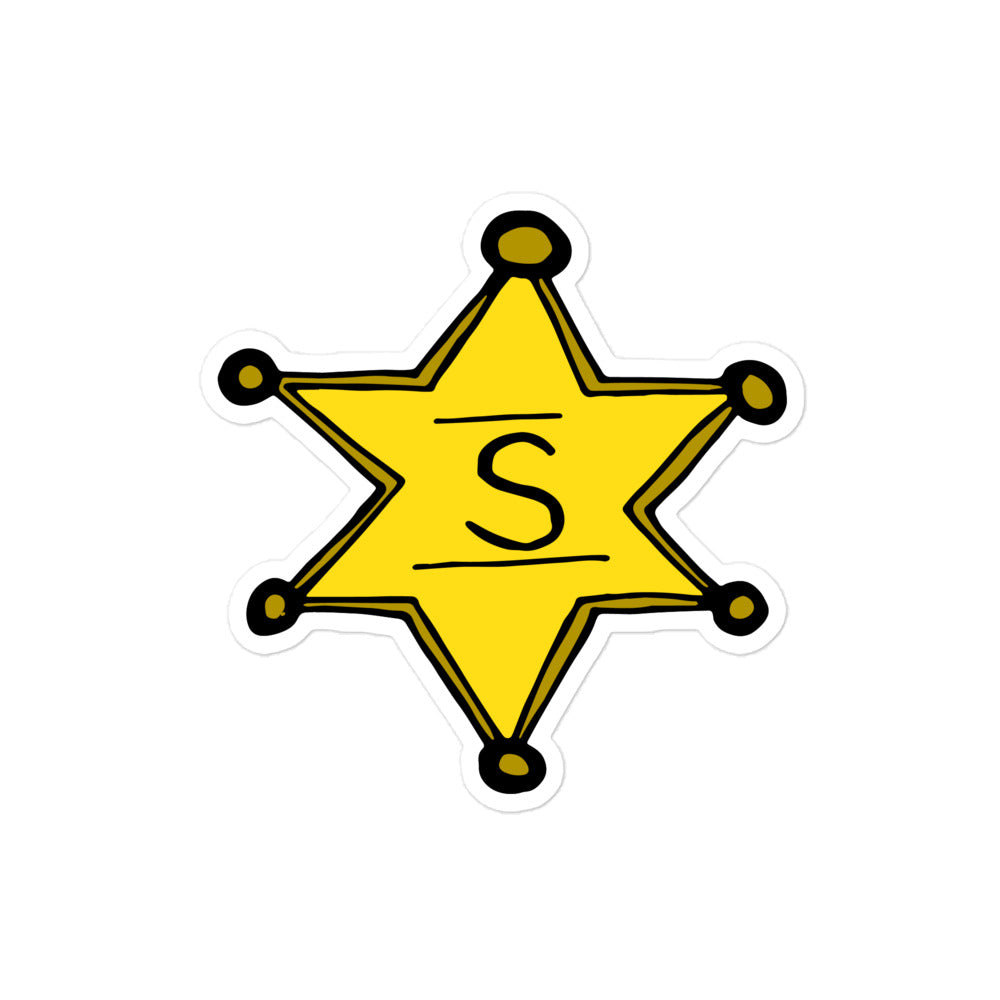 A photo of a yellow Sheriff's badge sticker with an "S" for Sheriff in the centre. 