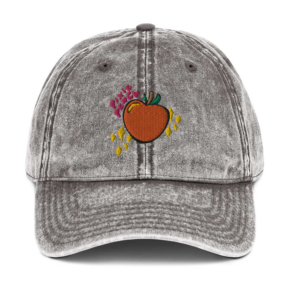 A photo of the front of a charcoal grey cotton twill cap, showcasing the Pixie Peach logo (pink text, orange peach with green leaves and a brown stalk, yellow sparkles and yellow reflective gleam on the peach). 